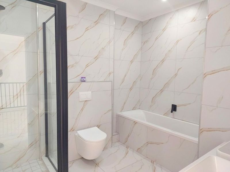 Modern bathroom featuring marble-look tiled walls and floors, a built-in bathtub, a wall-mounted toilet with concealed cistern, and a glass-enclosed shower.