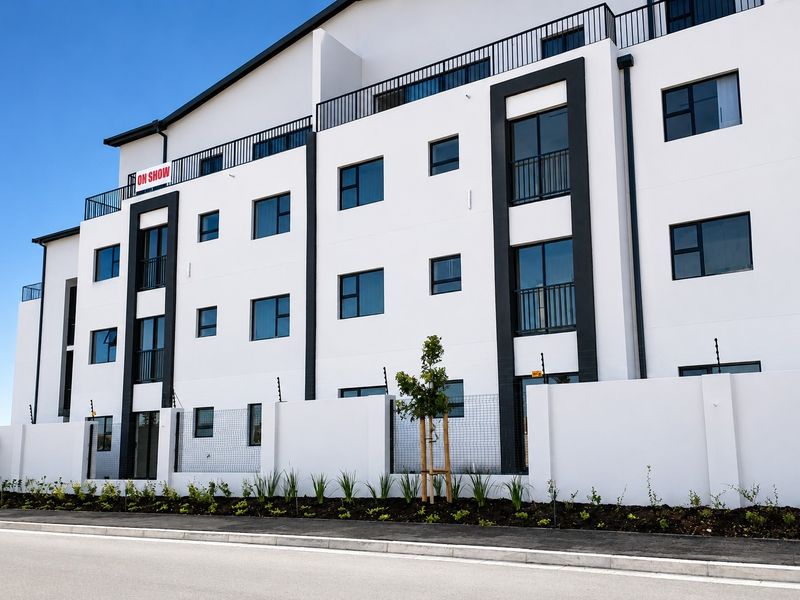 Modern multi-story townhouse exterior featuring clean white facade, dark accent detailing, balcony railings, and secure perimeter wall with electric fencing.