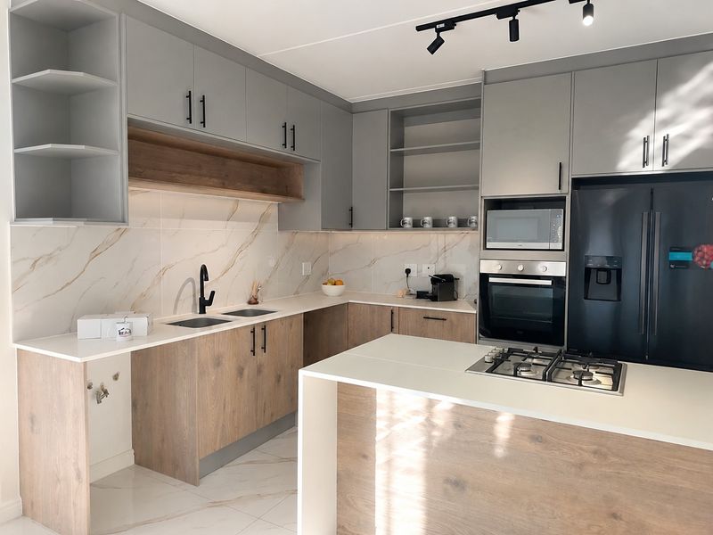 Modern kitchen featuring two-tone cabinetry, stone countertops, marble-look splashback, integrated appliances, and a central island with a gas cooktop.