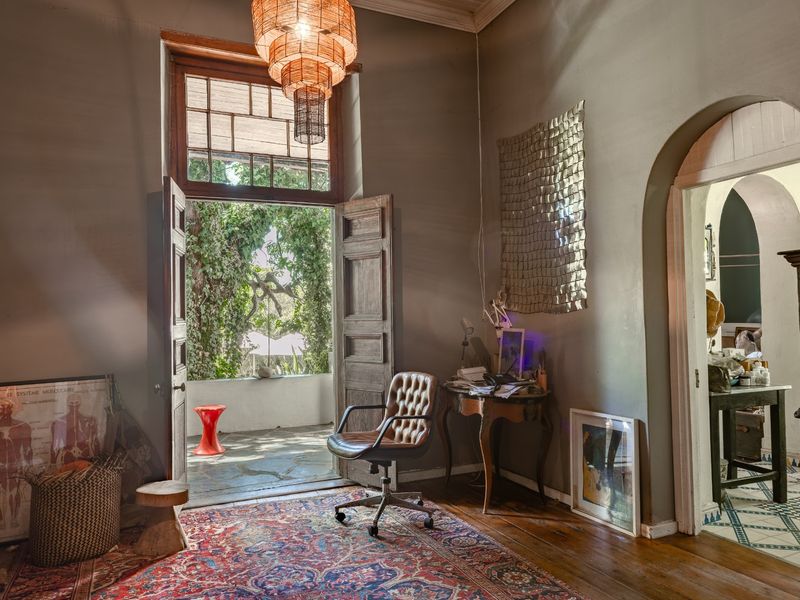 A characterful living space featuring original hardwood floors, an elegant arched doorway, and timber double doors opening onto a private patio area.