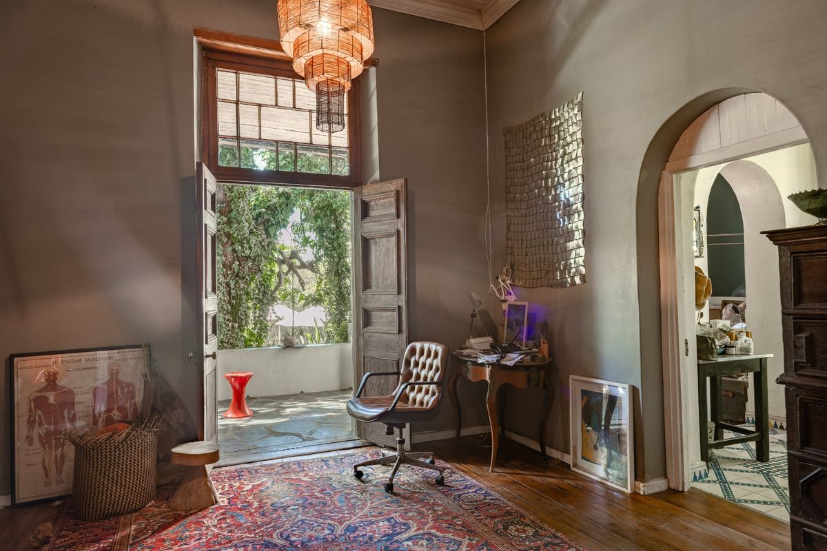 A characterful living space featuring original hardwood floors, an elegant arched doorway, and timber double doors opening onto a private patio area.