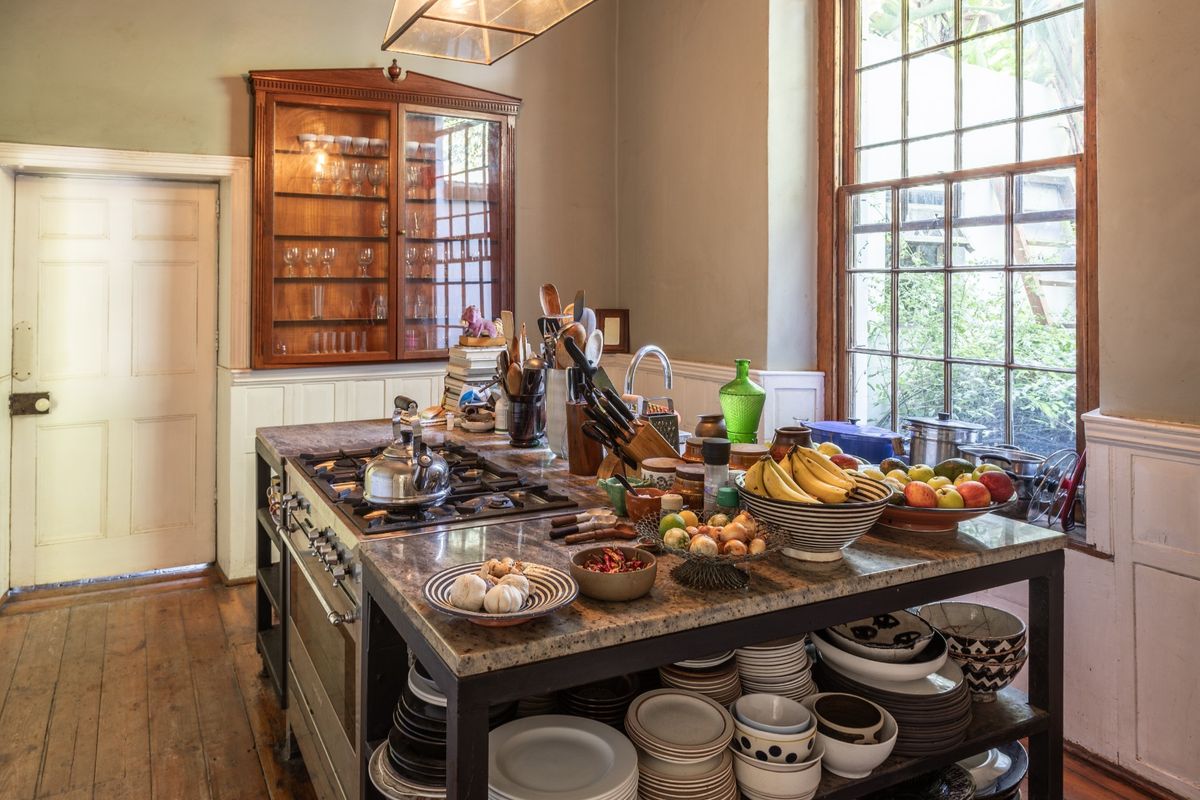 A characterful kitchen featuring a large central island with a stone countertop, integrated gas hob, oven, and classic timber flooring with wainscoting details.
