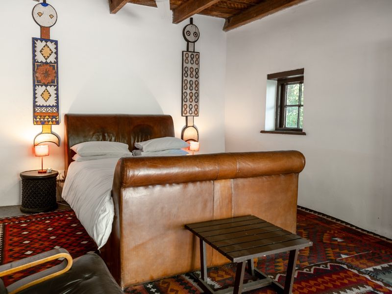 A rustic bedroom featuring exposed timber ceiling beams, white walls, and a small casement window, creating a cozy and character-filled sleeping space.