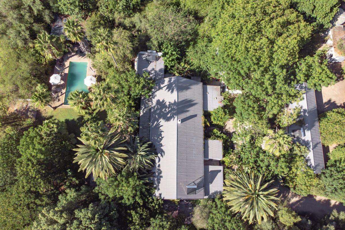 Aerial view of a farm property featuring a main residence with a metal roof, solar water heater, and a private swimming pool set in greenery.