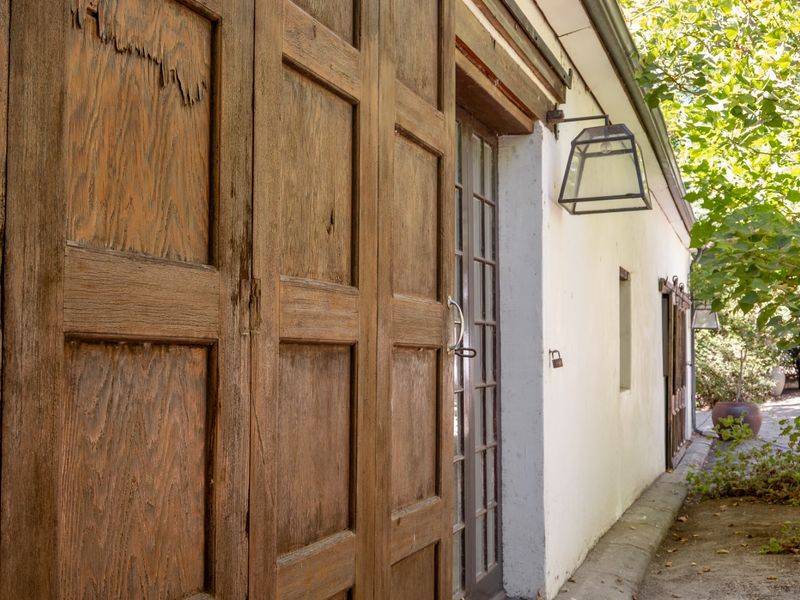 Exterior view of a rustic farm building featuring a large sliding wooden barn door, glass-paned french doors, and classic wall-mounted lantern lighting.