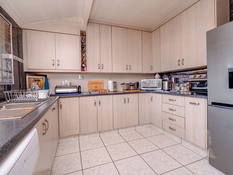 Functional kitchen featuring light wood-tone cabinetry, dark laminate countertops, tiled flooring, and a double basin sink with ample storage space.