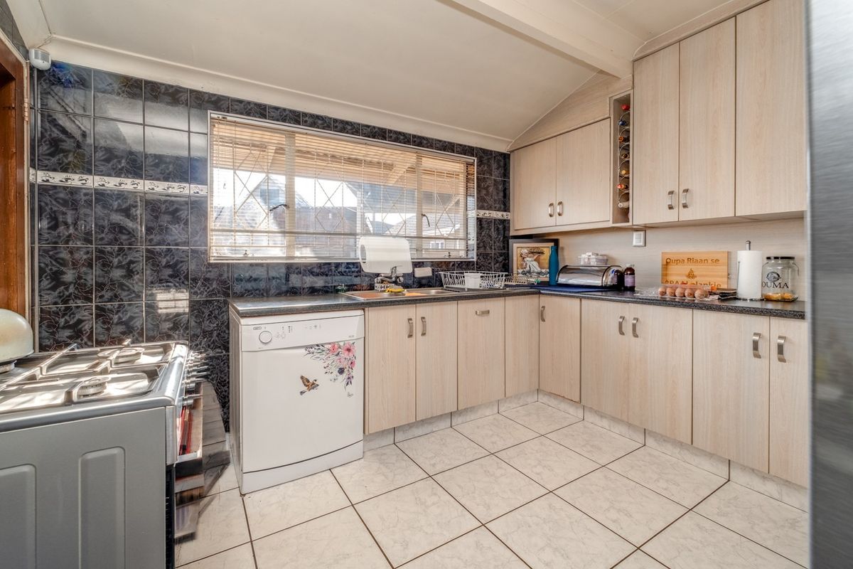 A functional kitchen featuring light wood-look cabinetry, dark granite countertops, dark tiled backsplash, and ceramic floor tiles with a window for natural light.