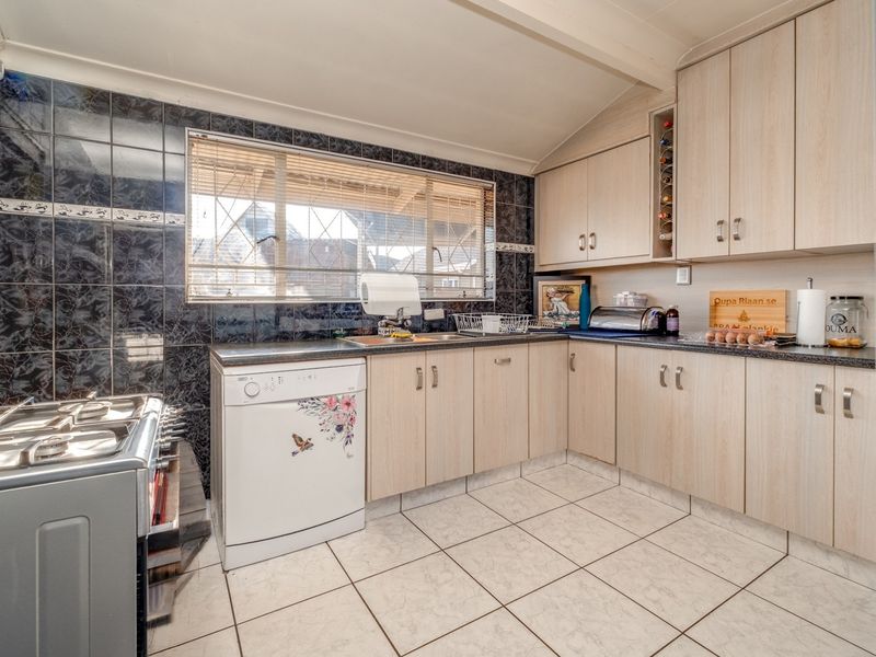 A functional kitchen featuring light wood-look cabinetry, dark granite countertops, dark tiled backsplash, and ceramic floor tiles with a window for natural light.