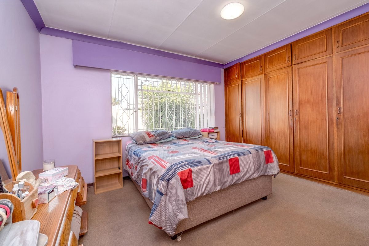 A bedroom featuring built-in wooden cupboards, carpeted flooring, and a window fitted with a security gate.