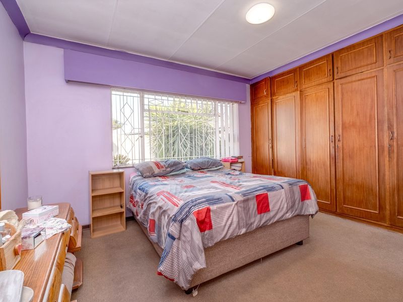 A bedroom featuring built-in wooden cupboards, carpeted flooring, and a window fitted with a security gate.