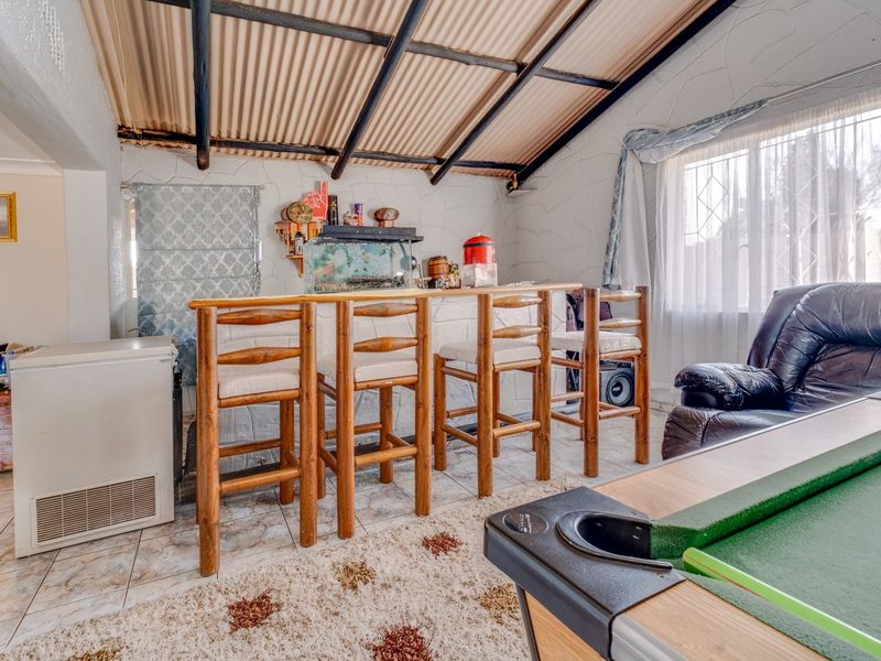 A rustic entertainment area featuring a built-in bar counter, tiled flooring, and an exposed beam ceiling with corrugated roof sheeting.