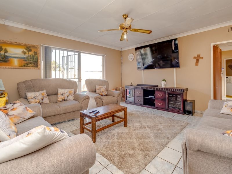 A comfortable living room featuring tiled flooring, a ceiling fan, and a sliding glass door with security gate providing access to the exterior.