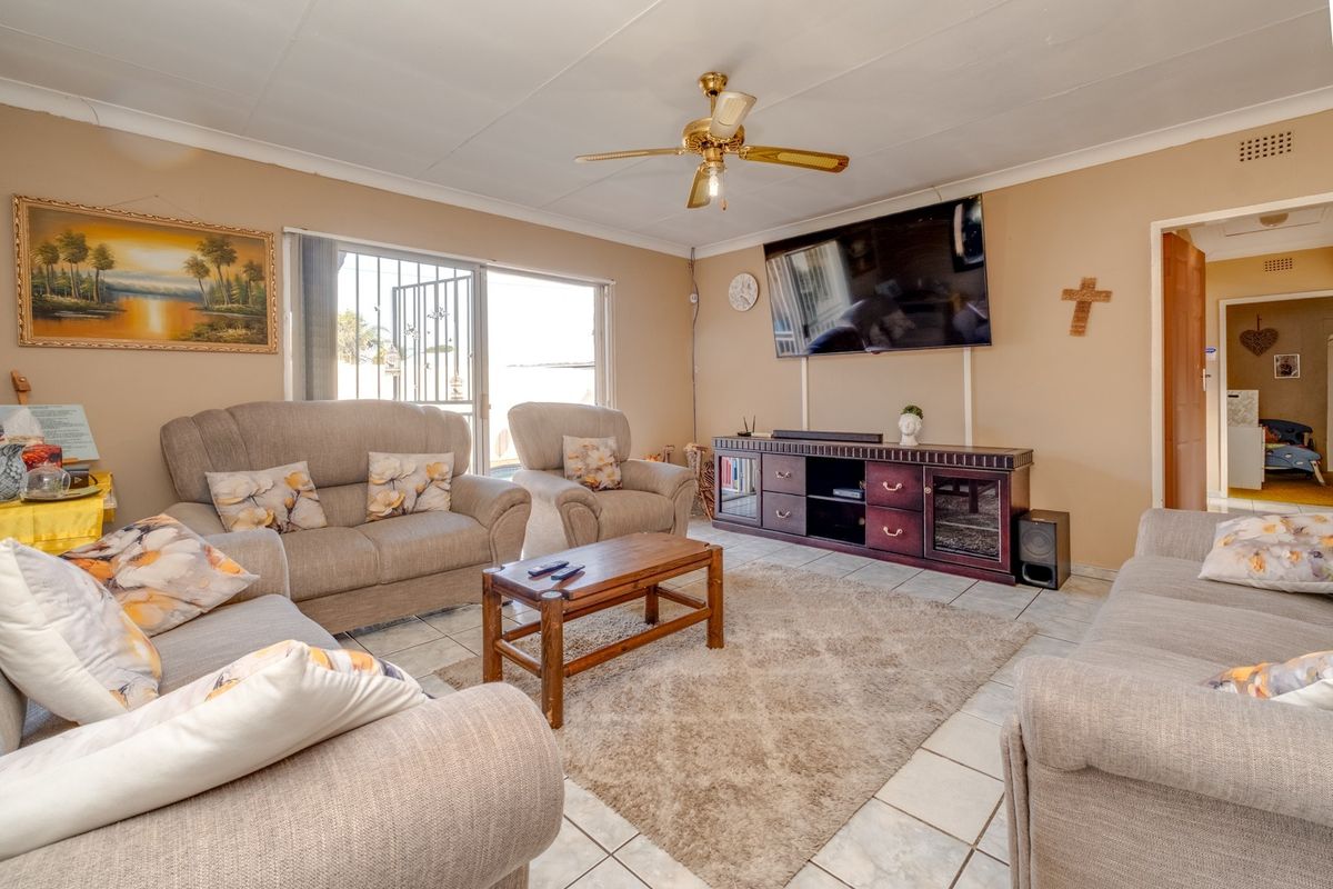 A comfortable living room featuring tiled flooring, a ceiling fan, and a sliding glass door with security gate providing access to the exterior.