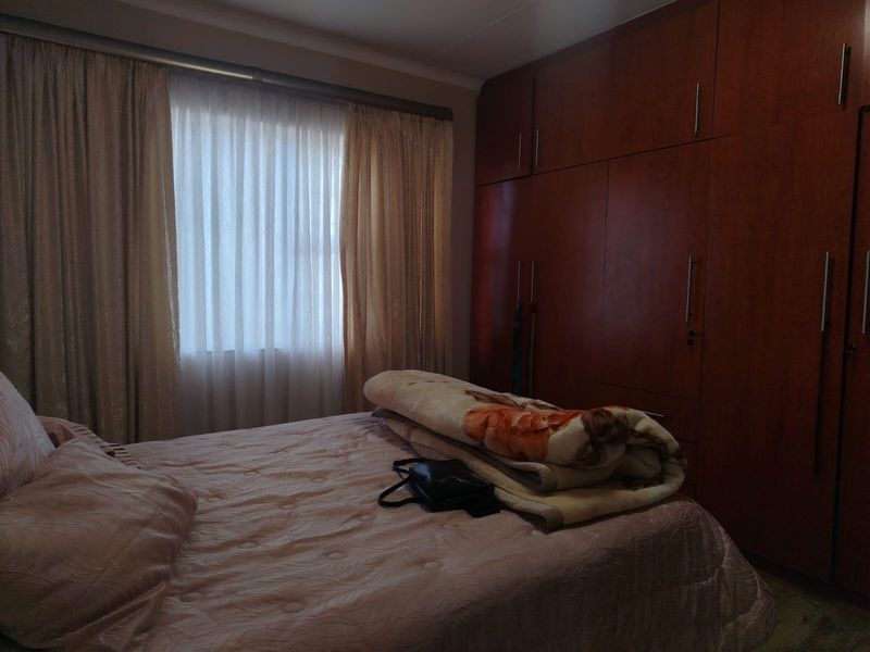 A bedroom featuring extensive floor-to-ceiling built-in wooden cupboards and large windows with installed curtain rails.