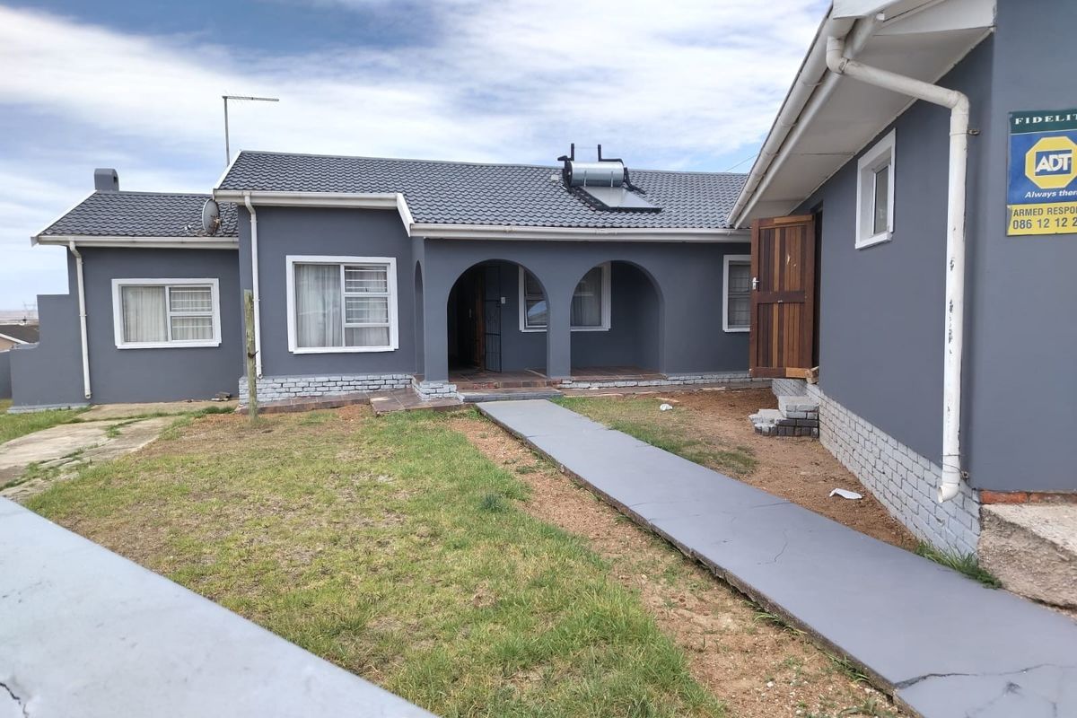 Rear view of a grey-painted house featuring an arched covered patio, solar water heating system, and a concrete walkway leading to the entrance.