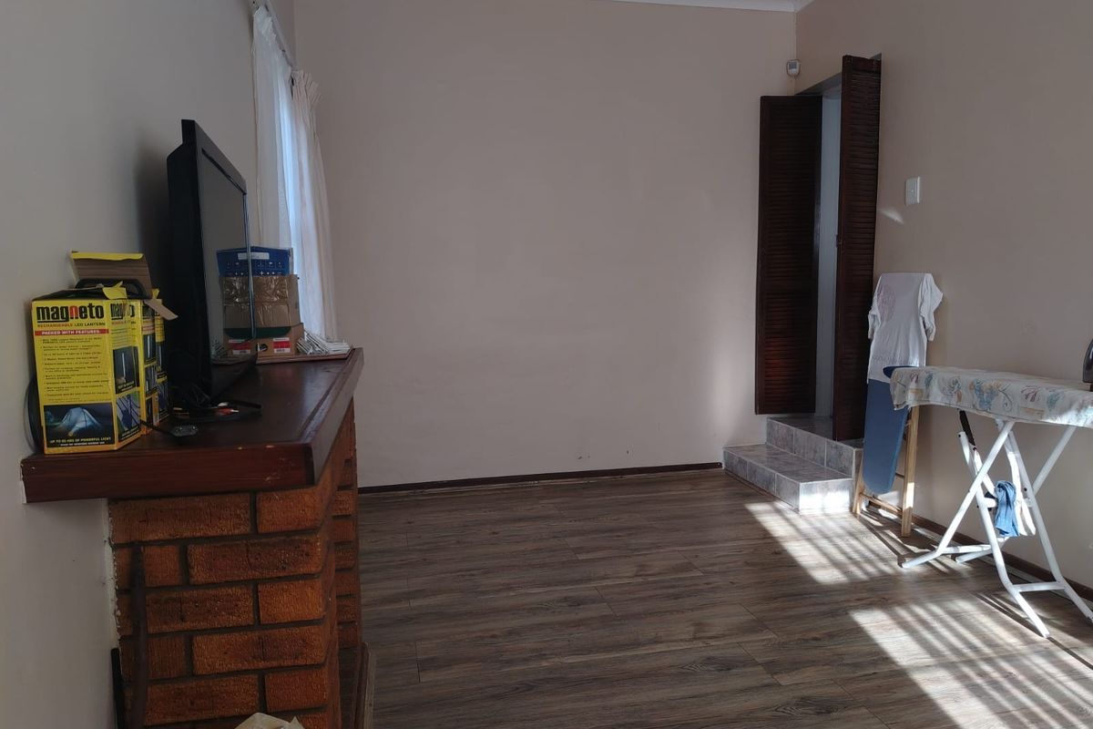 A living room featuring a brick fireplace and laminate flooring, with a louvered door leading to an adjacent space.