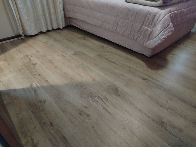 A bedroom featuring light-toned wood-look laminate flooring and neutral curtains.