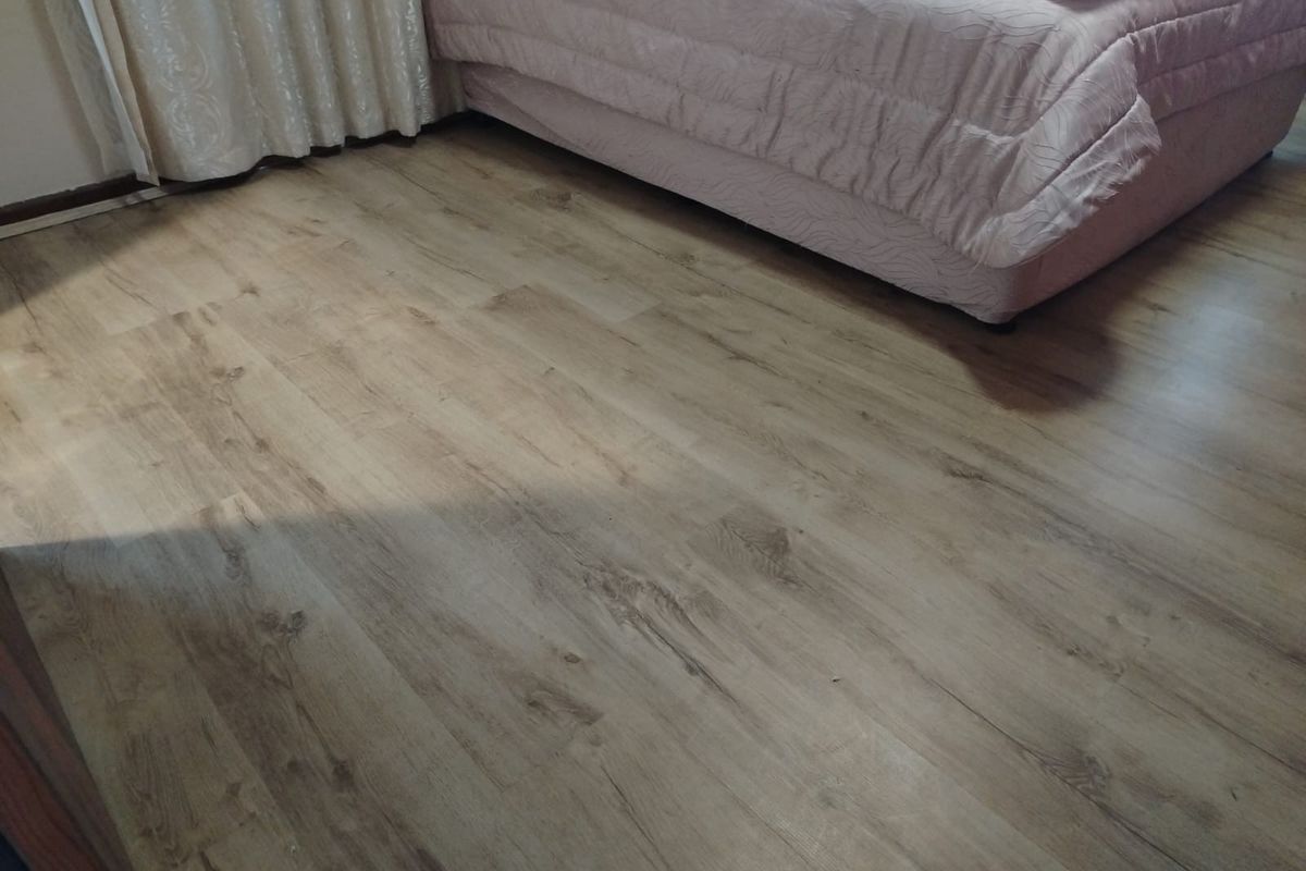 A bedroom featuring light-toned wood-look laminate flooring and neutral curtains.