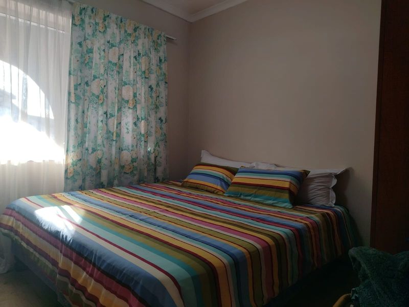 A standard bedroom featuring neutral wall finishes and natural light through a window with curtain fixtures.