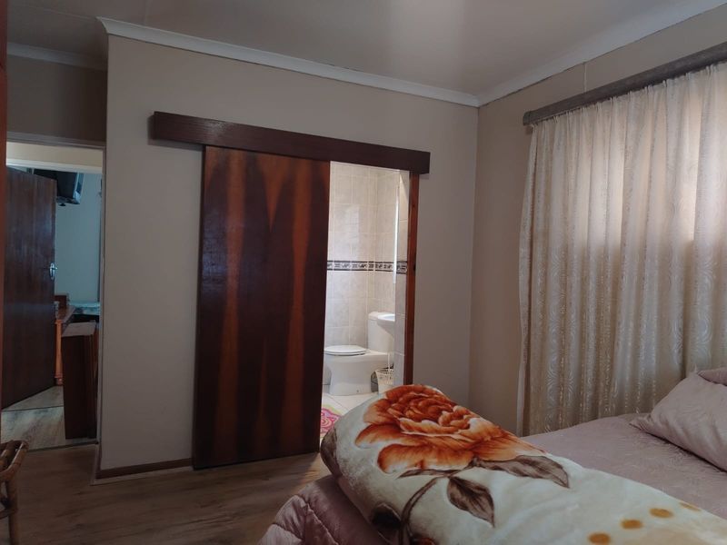 A bedroom featuring laminate flooring and a sliding wooden door leading to an en-suite bathroom with tiled walls.