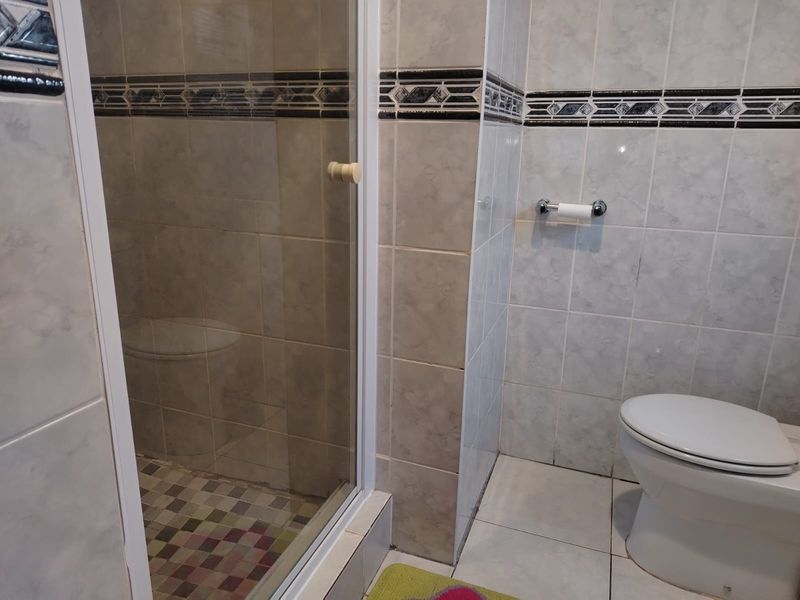 A functional bathroom featuring a glass-enclosed shower, tiled walls with decorative border, and a standard toilet.