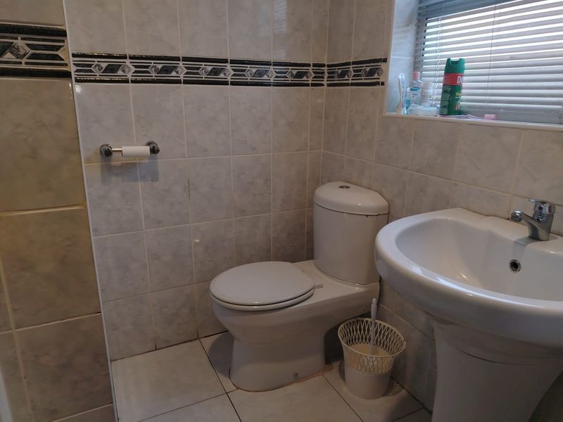A functional bathroom featuring a pedestal basin, toilet, and neutral tiled walls with a decorative border.