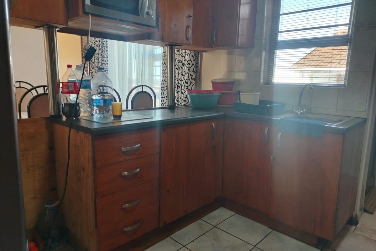 A functional kitchen featuring wooden cabinetry, laminate countertops, a stainless steel sink, and tiled flooring, offering a classic layout with potential for modernization.