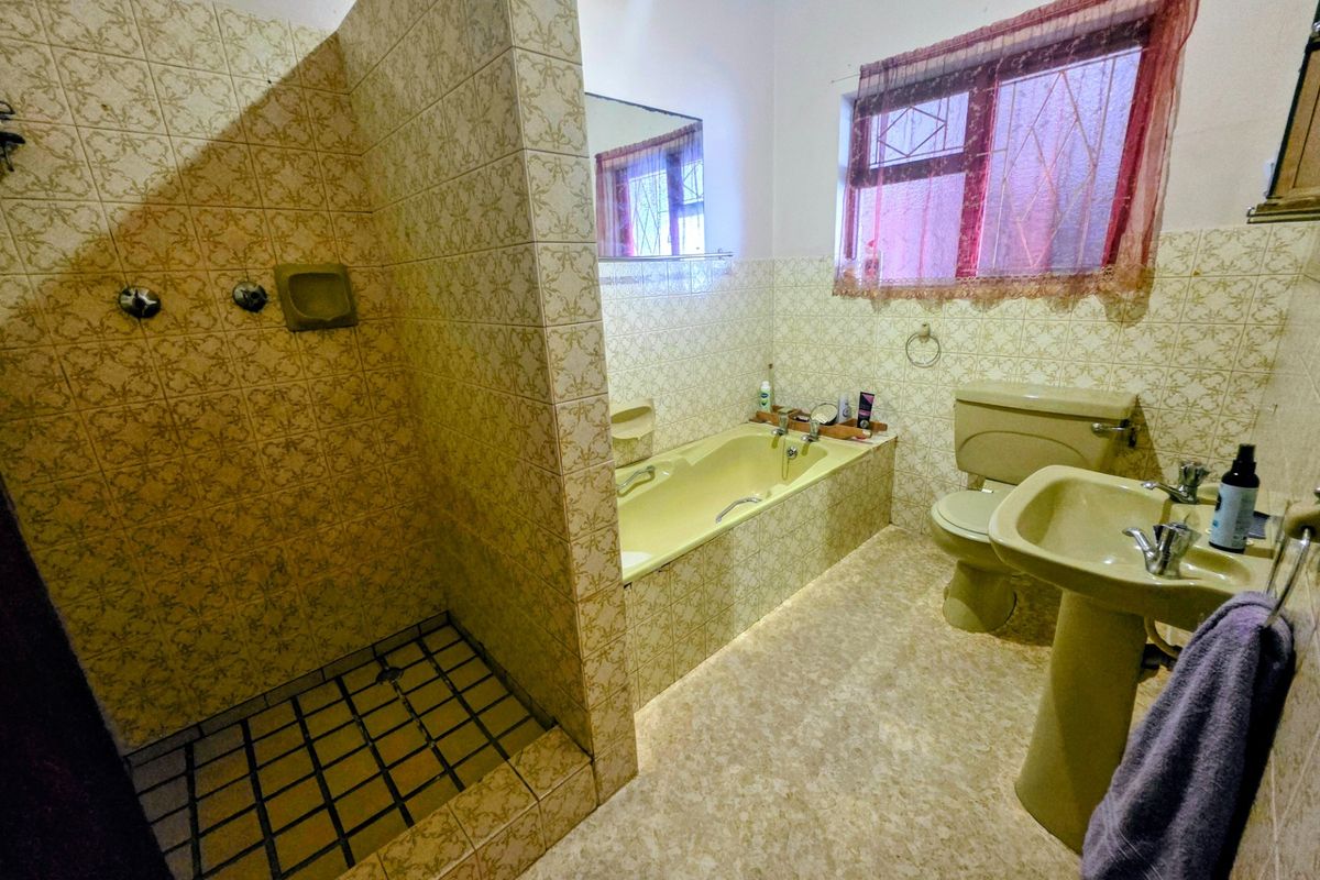 A dated bathroom featuring a walk-in shower, built-in bathtub, pedestal basin, and toilet with original patterned wall tiling.