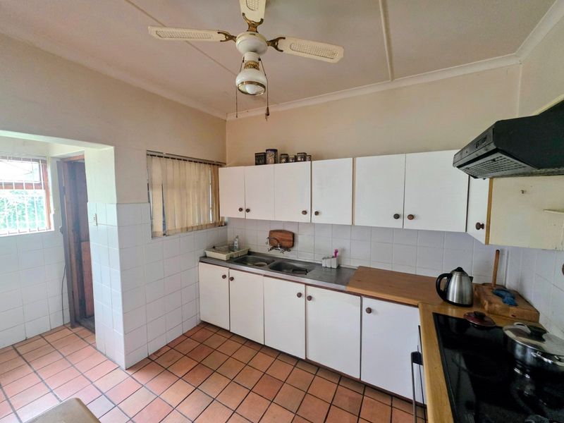 A functional kitchen featuring white cabinetry, tiled splashbacks, ceramic floor tiles, and a built-in cooktop with an extractor fan.