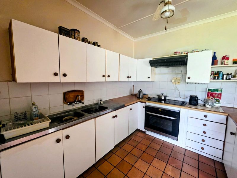 A functional kitchen featuring white cabinetry, laminate countertops, a built-in oven with electric cooktop, and tiled flooring.