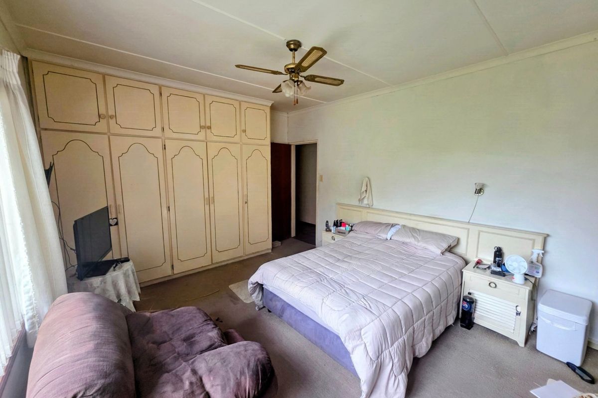 Spacious bedroom featuring extensive built-in cabinetry, a ceiling fan, and integrated headboard with matching bedside tables, offering potential for modernization.