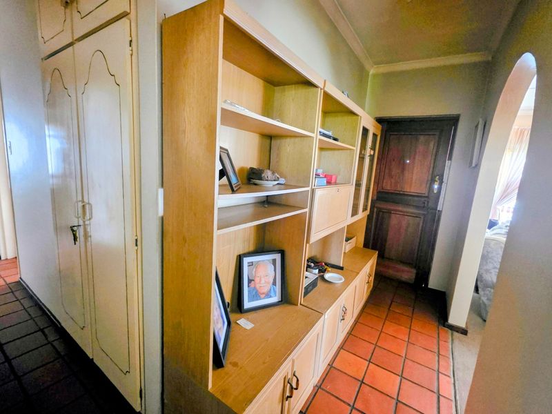 A hallway featuring terracotta floor tiles, built-in storage cupboards, and a traditional wooden door leading to an adjacent room.