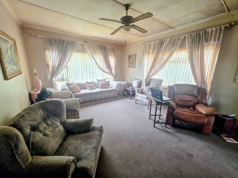 Spacious living room featuring a ceiling fan and large windows with vertical blinds, offering a blank canvas for modernization and renovation.