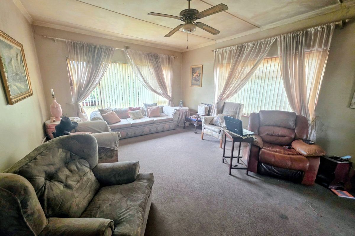Spacious living room featuring a ceiling fan and large windows with vertical blinds, offering a blank canvas for modernization and renovation.