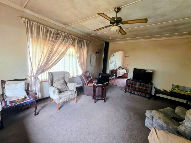 A living room featuring a ceiling fan, wood-burning stove, and an arched entryway, showing signs of wear and requiring cosmetic updates.