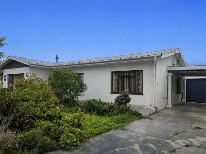 Front exterior view of a single-story house featuring a metal roof, attached carport, garage, and a front garden with a concrete driveway.