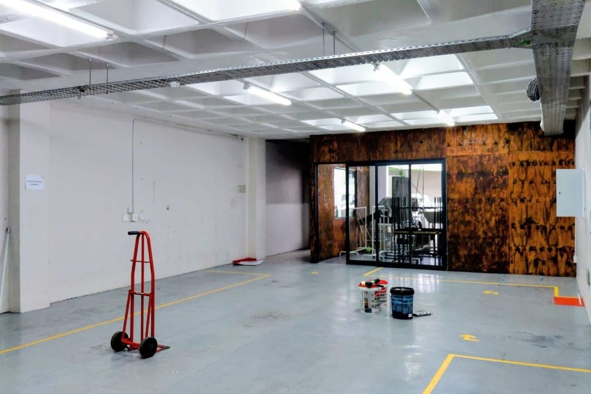 Spacious industrial utility area featuring a waffle slab ceiling, exposed cable management, epoxy flooring, and a glass-partitioned office or storage section.