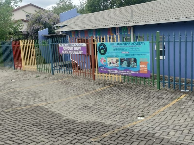Front exterior view of the property featuring a paved driveway, metal security fencing, and painted building facade currently utilized as a school.