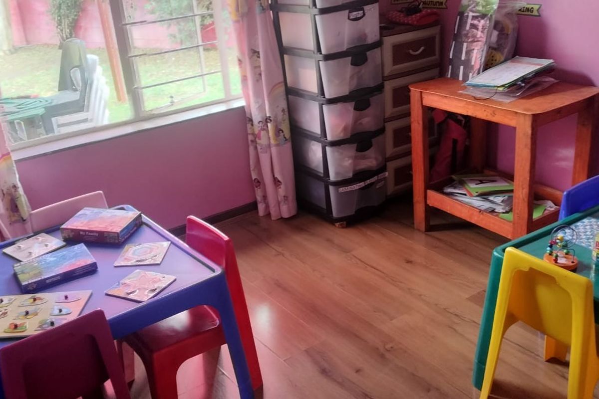 A functional bedroom space featuring laminate flooring and a large window with security bars, currently utilized as a children's play or learning area.