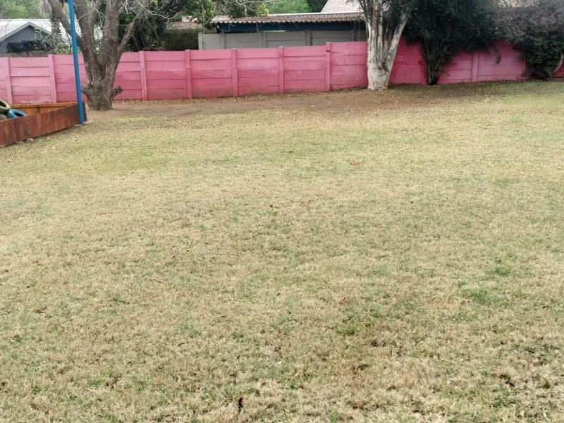 A spacious outdoor garden area featuring a large lawn, precast concrete boundary wall, and existing playground equipment.