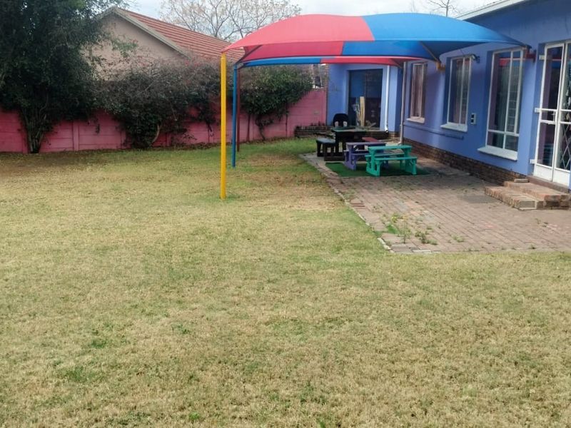 Rear exterior view featuring a paved patio area with a shade sail, a large lawn, and perimeter boundary walls.