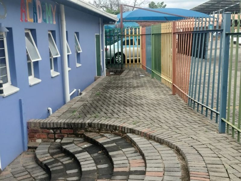Exterior rear area featuring a paved walkway, brick steps, and colorful metal security fencing alongside the building structure.