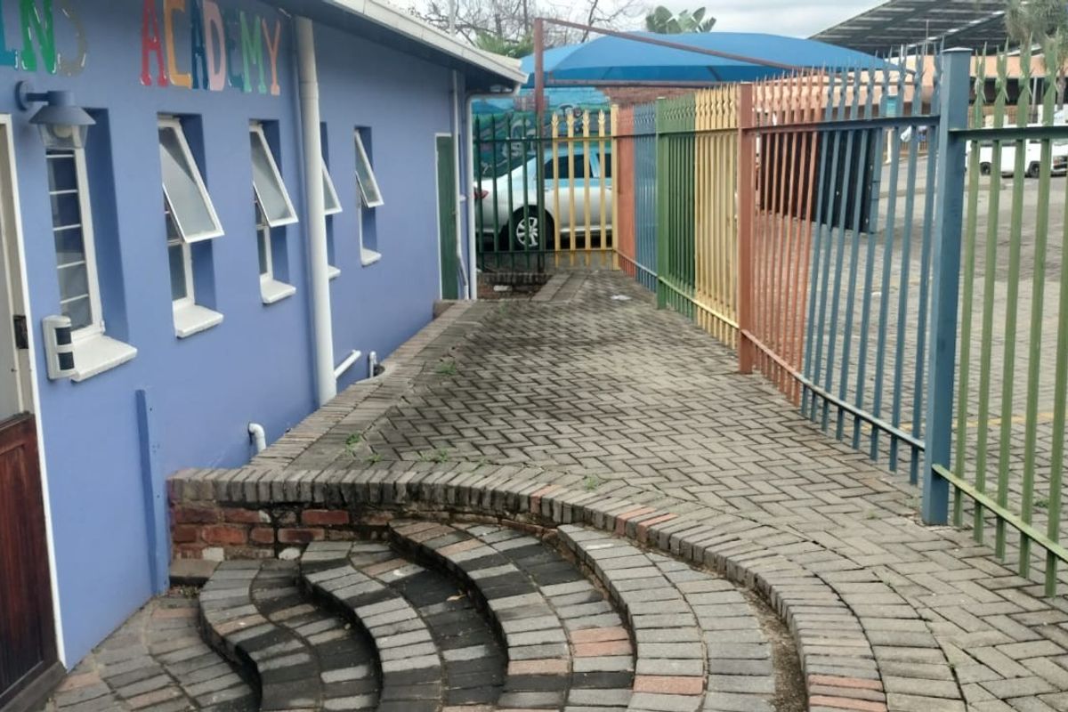 Exterior rear area featuring a paved walkway, brick steps, and colorful metal security fencing alongside the building structure.
