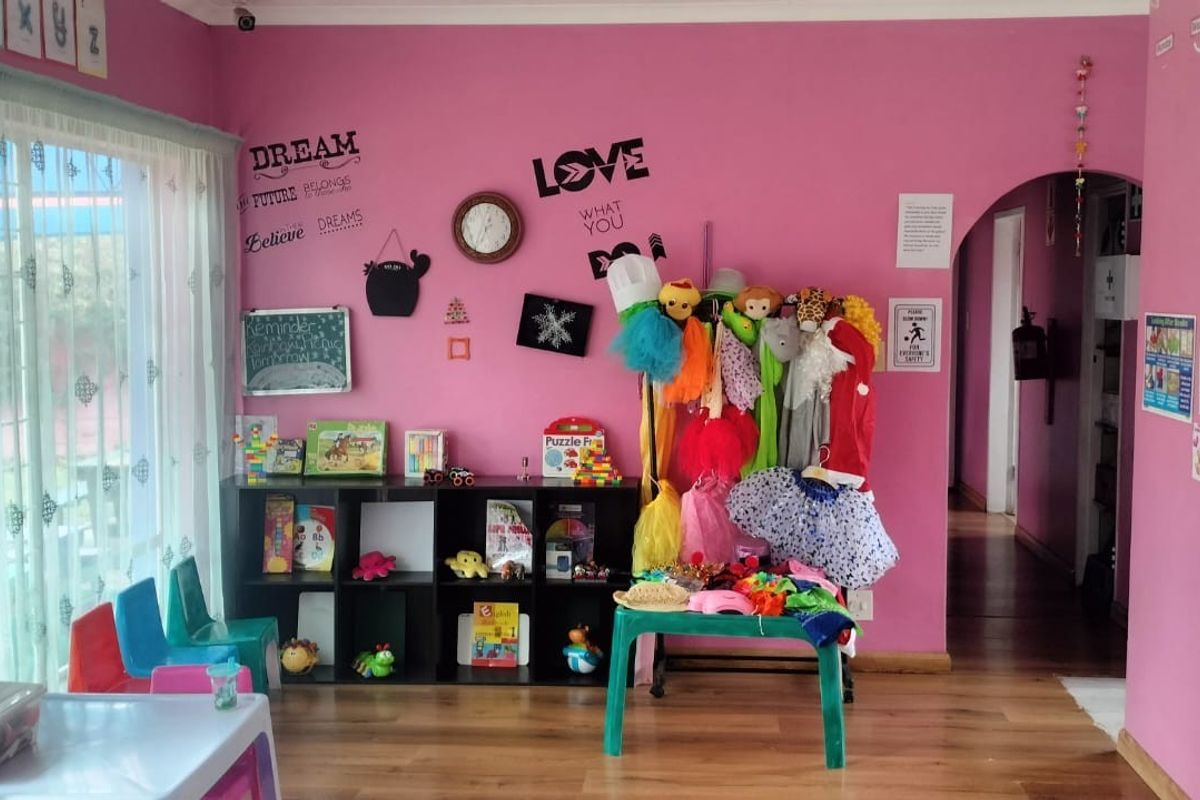 A brightly painted interior space currently utilized as a classroom, featuring laminate flooring, an arched doorway, and a sliding glass door with security gate.