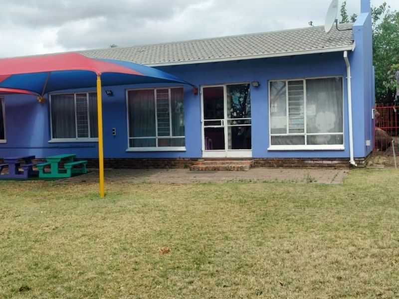 Rear view of the property featuring a paved patio area with a shade sail, aluminium window frames, and a large garden space.