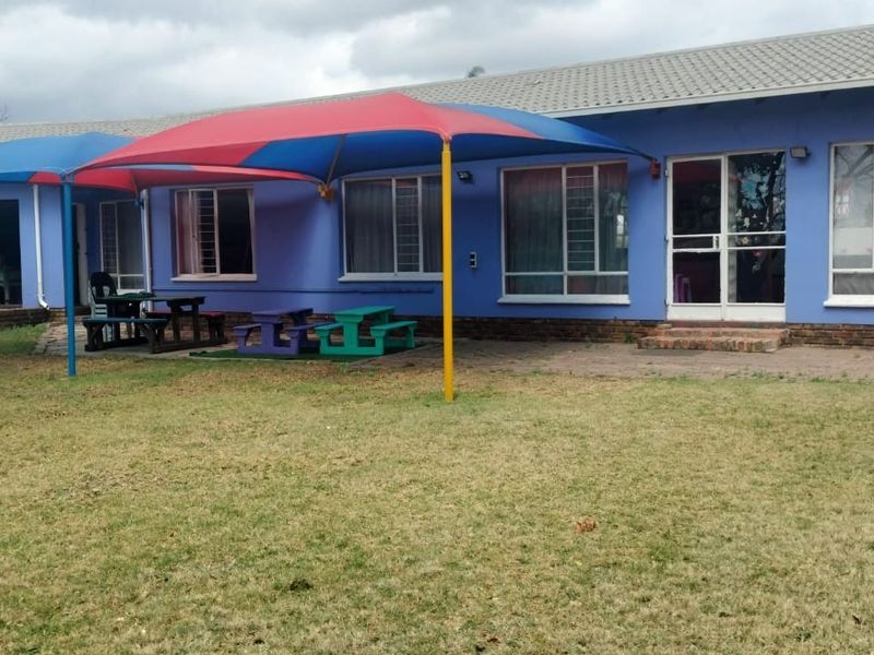 Rear view of the property featuring a paved patio area with shade sails, sliding glass doors, and a large grass garden.