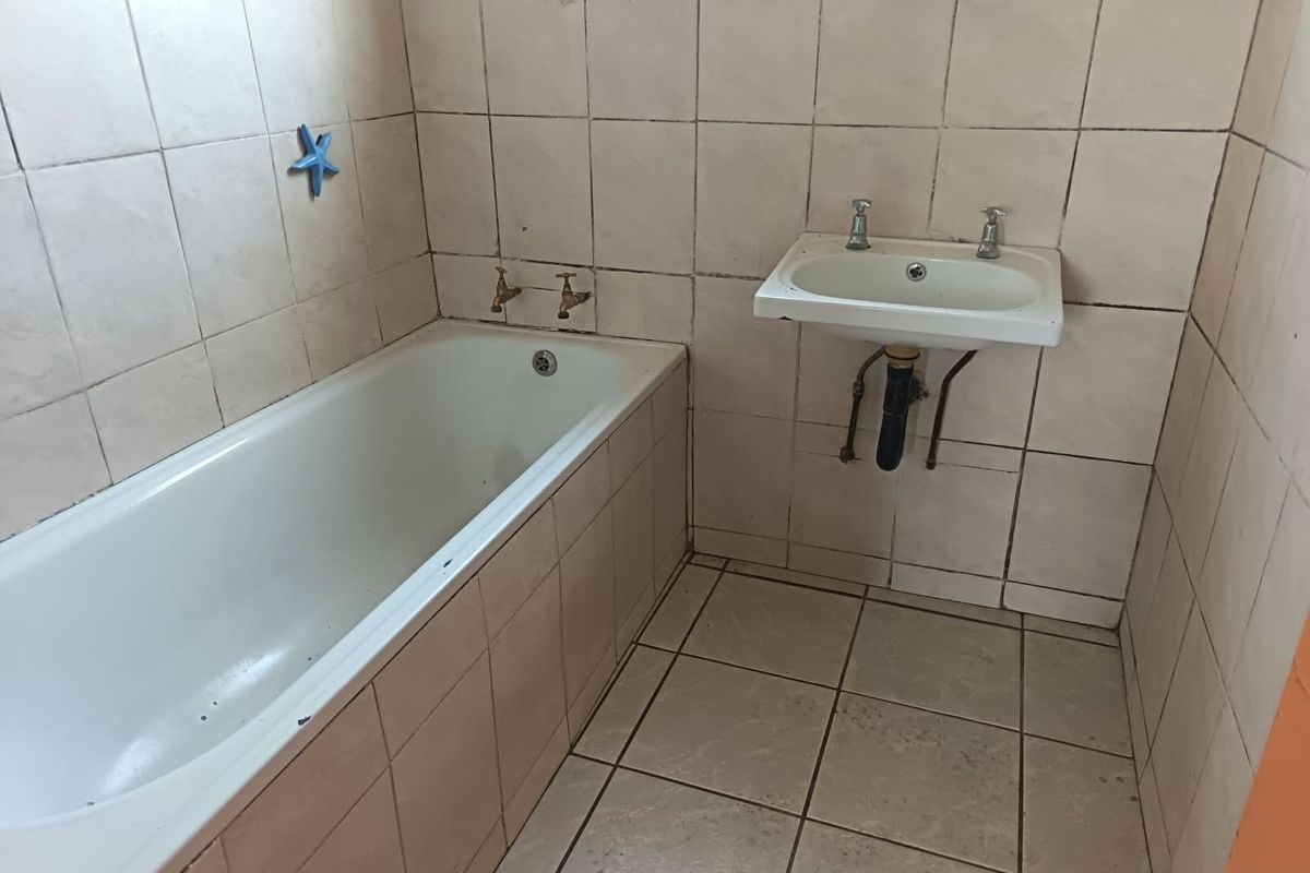 A dated bathroom featuring a built-in bathtub and wall-mounted basin with original ceramic tiling throughout, requiring renovation and modernization.