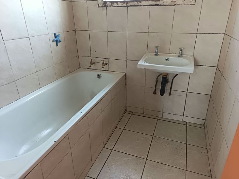 A dated bathroom featuring a built-in bathtub and wall-mounted basin with original ceramic tiling throughout, requiring renovation and modernization.
