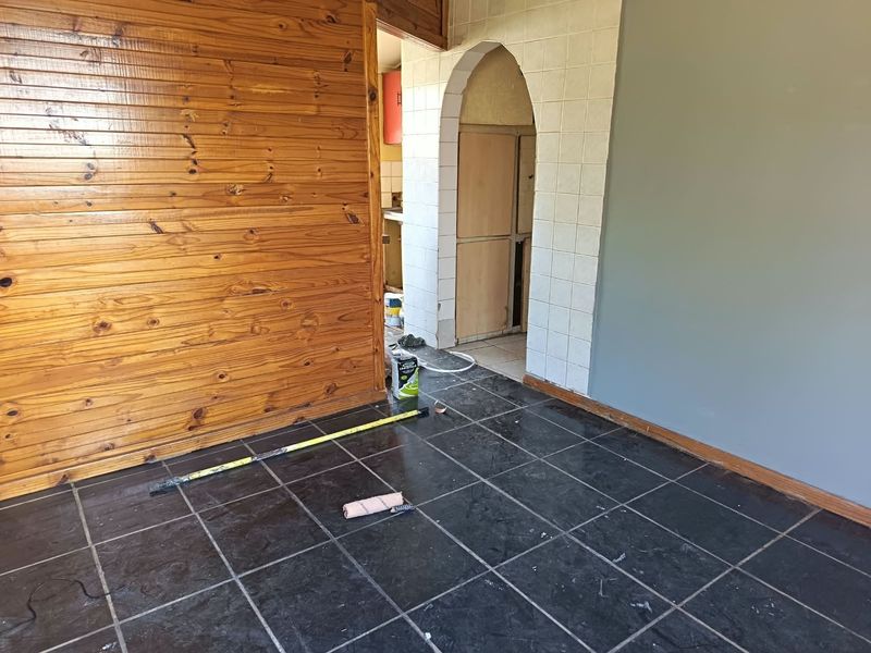 An interior living space currently undergoing renovations, featuring dark tiled flooring, timber wall paneling, and an arched entryway leading to an adjacent room.