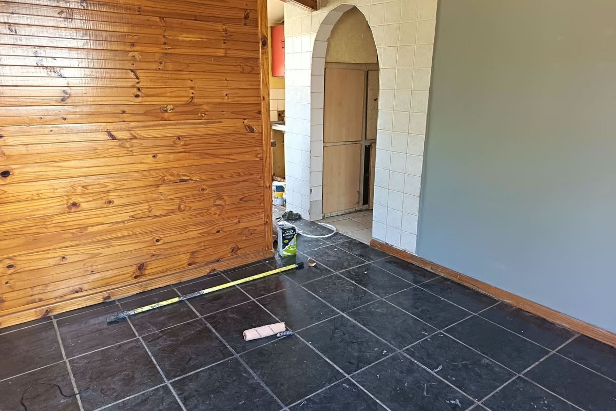 An interior living space currently undergoing renovations, featuring dark tiled flooring, timber wall paneling, and an arched entryway leading to an adjacent room.